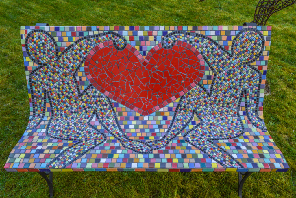 Banc en mosaïques multicolores. 2 personnages qui tiennent un grand coeur rouge.