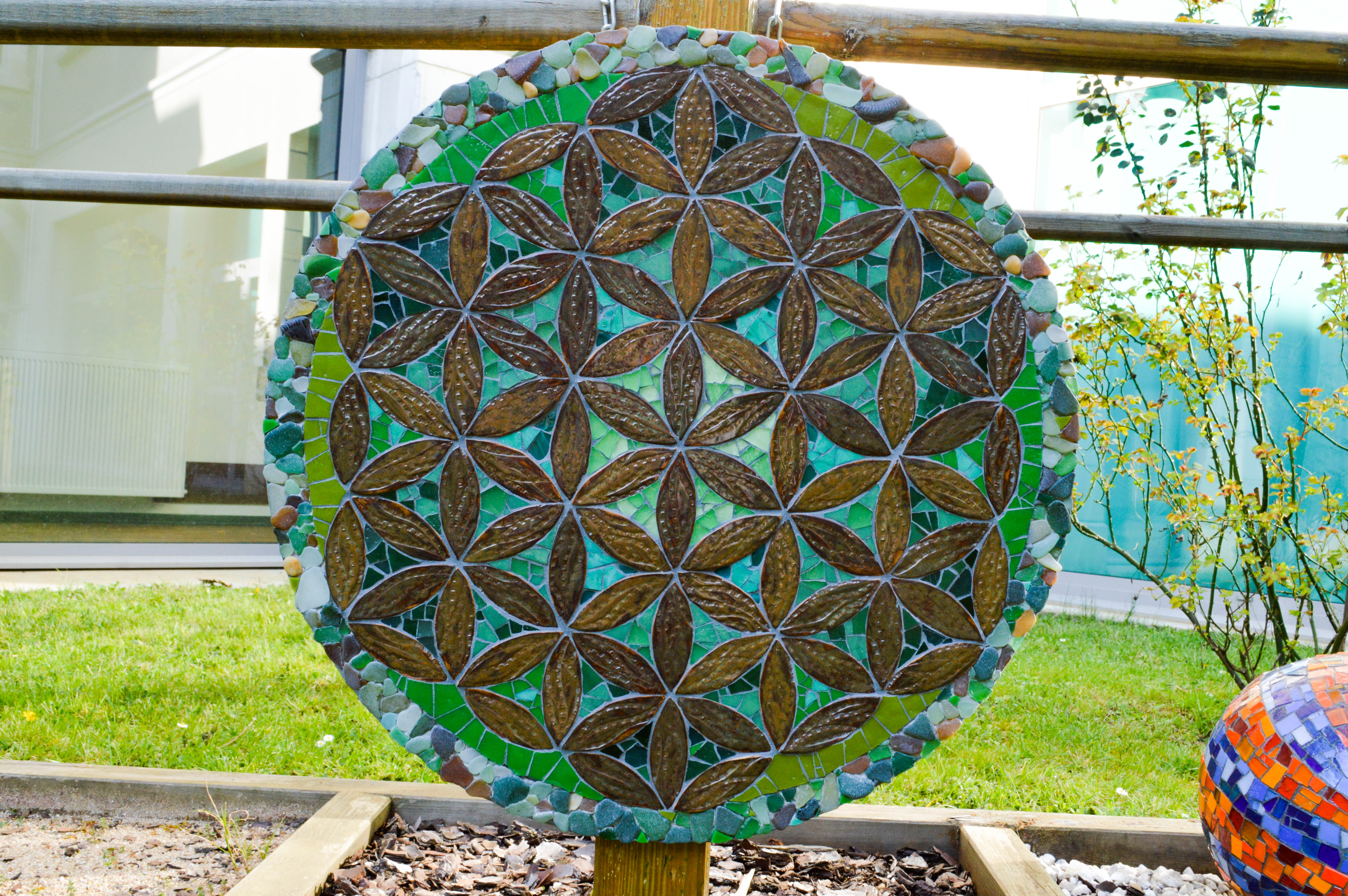 Mandala végétal réalisé avec des pétales en céramique, du verre, et des pierres de laplage, dan les couleurs verts.